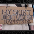 A placard, held by a woman wearing a white dress but whose face we cannot see: *My skirt doesn't cause rape - rapists do*