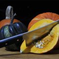An assortment of pumpkins in different colours. One has been halved and a cleaver is stuck deeply into its flesh.