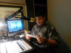 Young white man wearing headphones reads from script into radio mic.