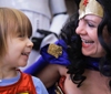 Woman in Wonder Woman costume laughs with child in WW shirt.