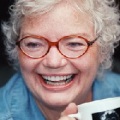 A middle aged pale skinned woman laughing unabashedly, holding a mug