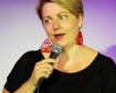 Middle aged white woman speaking into hand-held microphone.