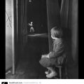 B&W photo of a toddler girl on a stool watching a woman on stage in the distance.